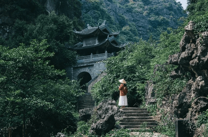 An adventurous traveler standing at the gate of Am Tien Pagoda looking down at the winding river valley below