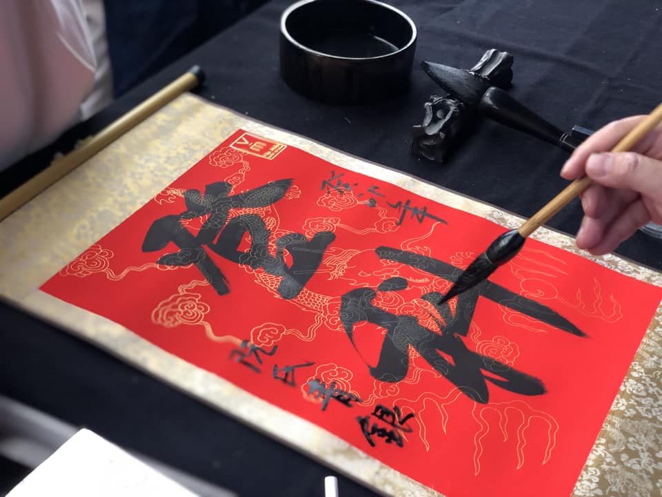 A scholar writing lucky calligraphy (Xin Chữ) during the vibrant Tết Lunar New Year celebrations at the temple.