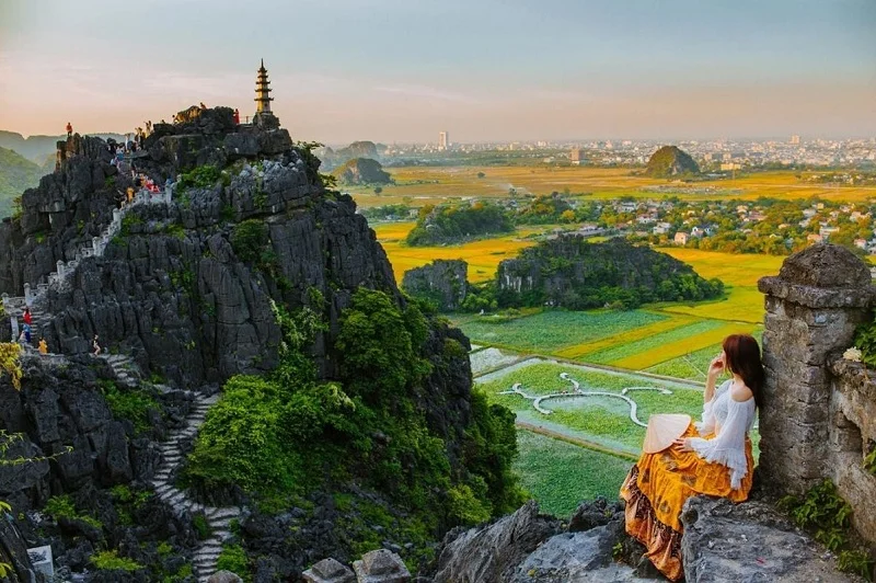 An adventurous traveler standing beside the iconic dragon shrine on the peak of Mua Cave at golden hour.