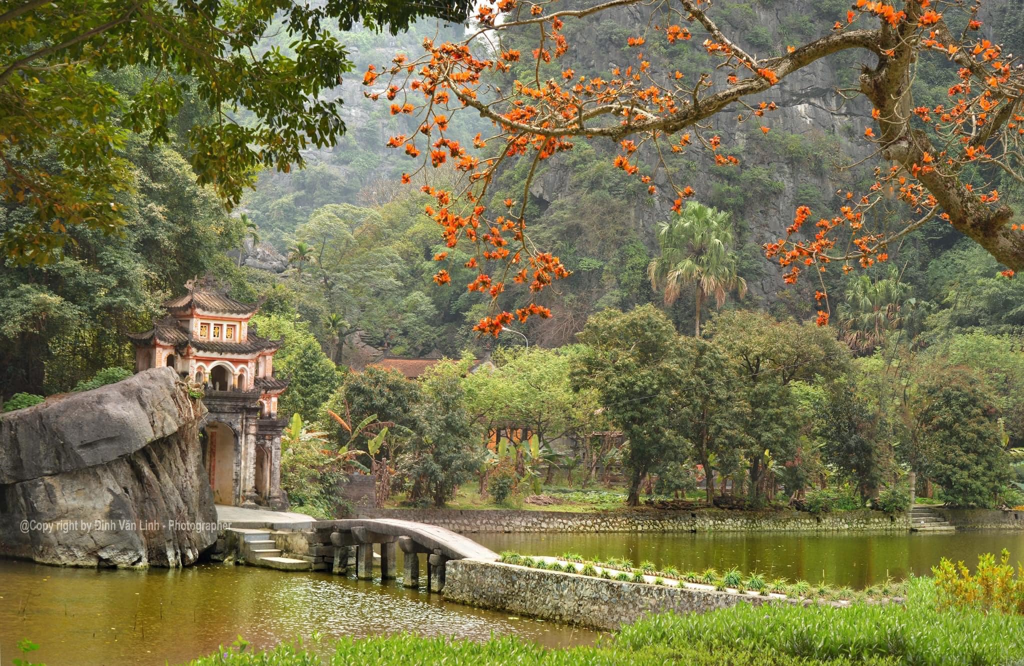 An international traveler walking across the iconic stone bridge leading into the mountain gate of Bich Dong Pagoda.