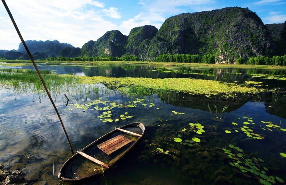 A traditional bamboo sampan gliding across the reflective waters of the vast wetland.