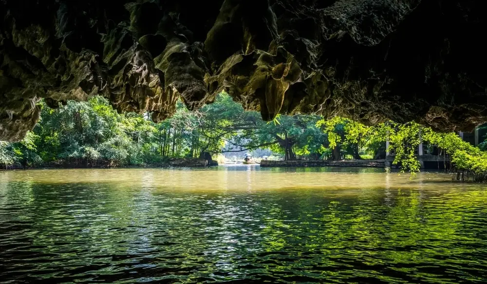 A boat entering the darkness of Hang Bong (Shadow Cave), showcasing the inner stalactites.